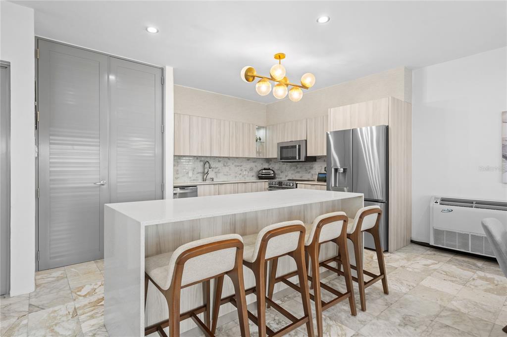 A modern kitchen features light wood cabinetry, a white quartz island, and three bar stools — 115 HARBOUR DRIVE UNIT 8, HUMACAO, PR
