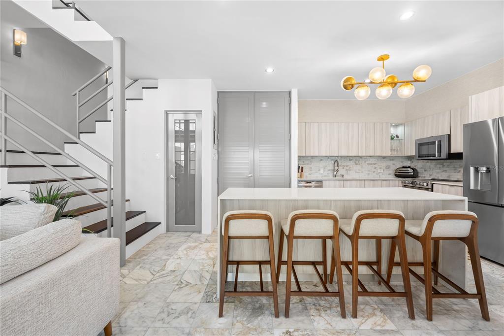 A modern kitchen features a marble-tiled floor, a central island with four stools, and stairs — 115 HARBOUR DRIVE UNIT 8, HUMACAO, PR