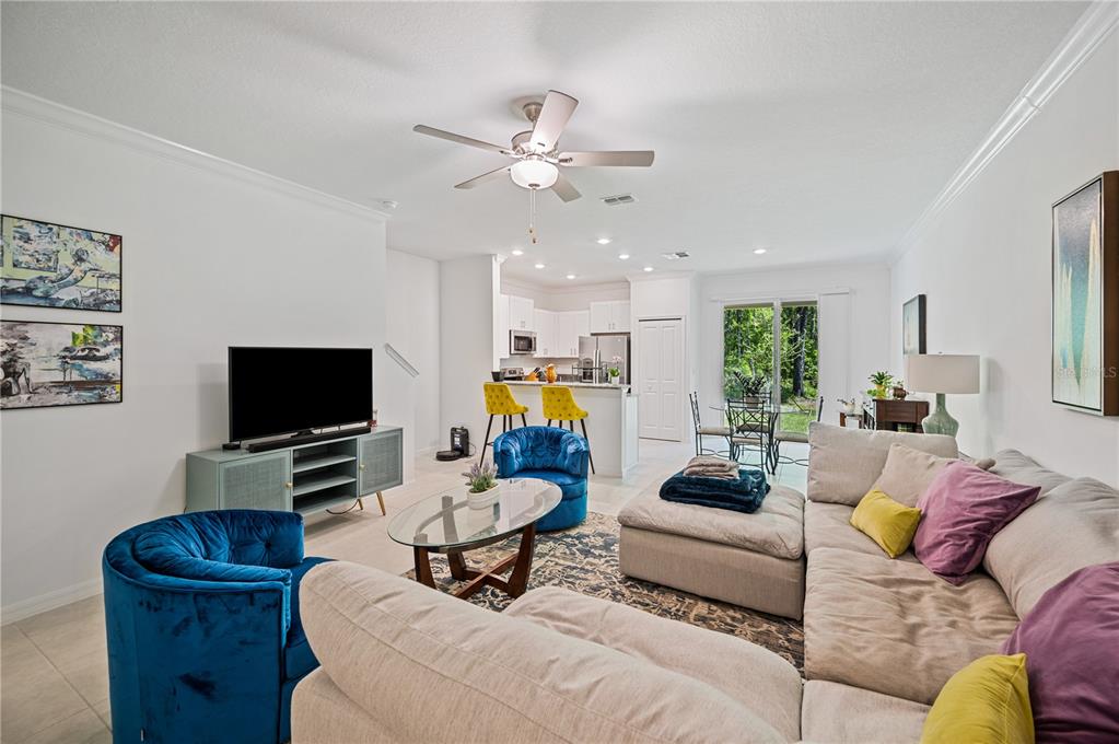 An open-concept living room features a sectional sofa, blue armchairs, and an adjacent kitchen — 17399 NECTAR FLUME DRIVE, LAND O LAKES, FL