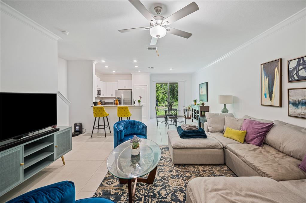 A living room with a sectional sofa, blue chairs, and an open kitchen with bar stools — 17399 NECTAR FLUME DRIVE, LAND O LAKES, FL