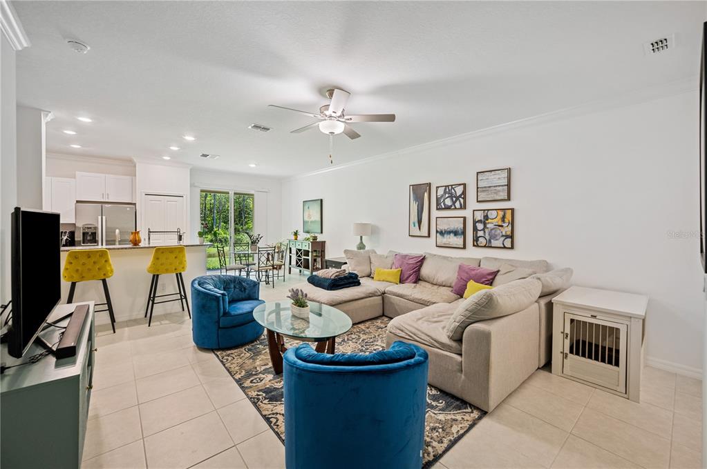 A living room features a sectional sofa, two blue armchairs, and an open kitchen area — 17399 NECTAR FLUME DRIVE, LAND O LAKES, FL
