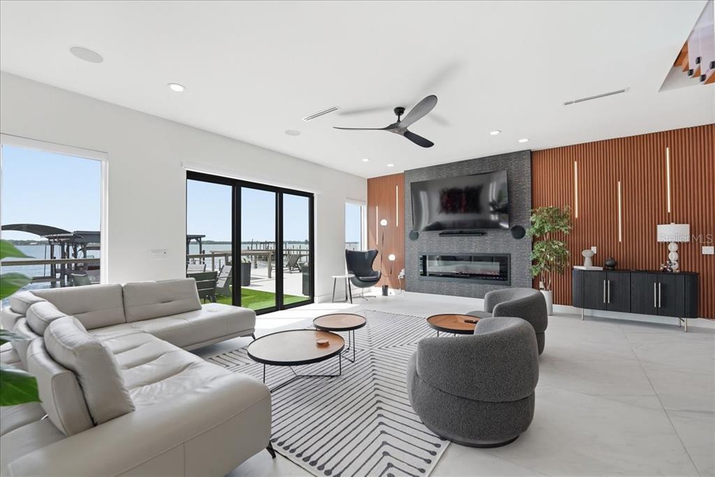 A modern living room features a fireplace, wall-mounted television, wood-slat paneling, and sliding glass doors — 2175 S TROPICAL TRAIL, MERRITT ISLAND, FL