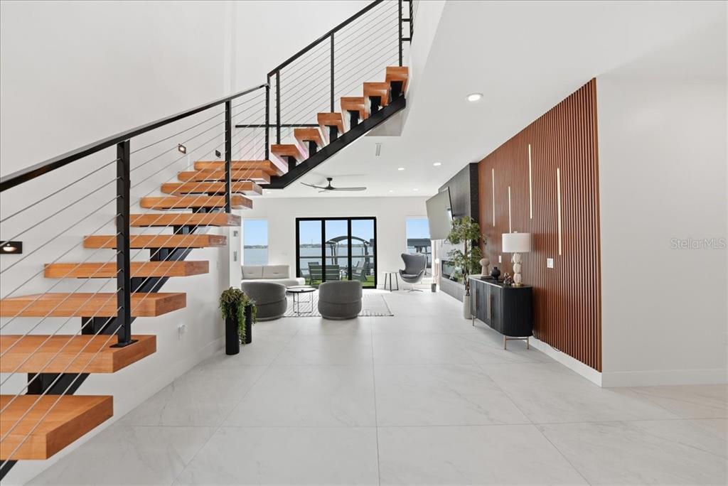 A modern living room features a floating wooden staircase, tile flooring, and a slat wall — 2175 S TROPICAL TRAIL, MERRITT ISLAND, FL