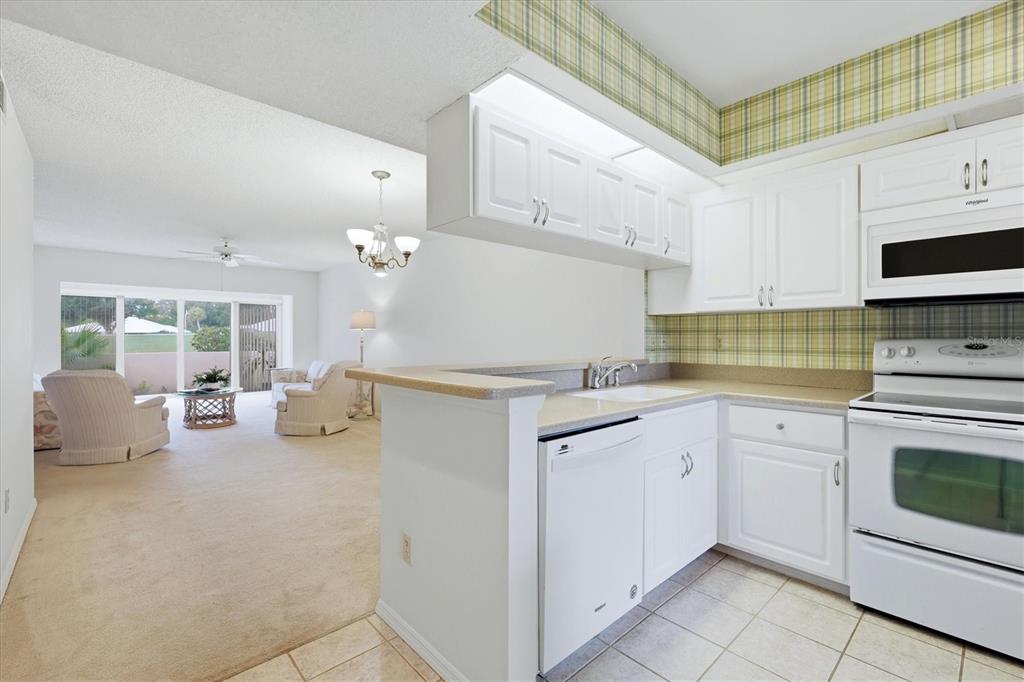 A living room features a beige sofa, matching armchairs, a glass-topped coffee table, and sliding doors — 421 CERROMAR TERRACE UNIT 370, VENICE, FL