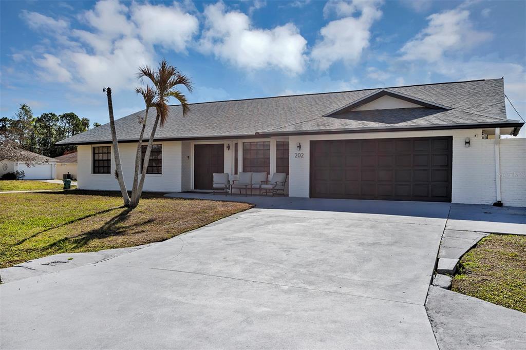 A single-story house with a white exterior, a dark garage door, and a palm tree — 202 SW HOLDEN TERRACE, PORT ST LUCIE, FL