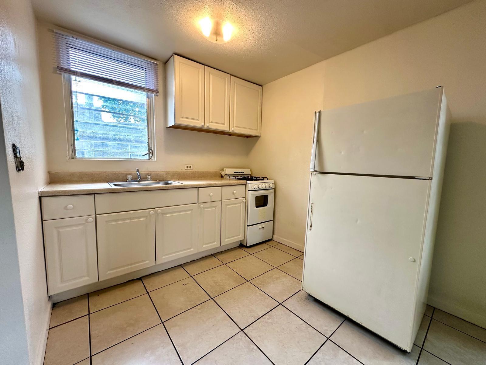 A small kitchen features white cabinets, a gas stove, a refrigerator, and tiled flooring — 610 33rd Street, West Palm Beach FL 33407, WEST PALM BEACH, FL