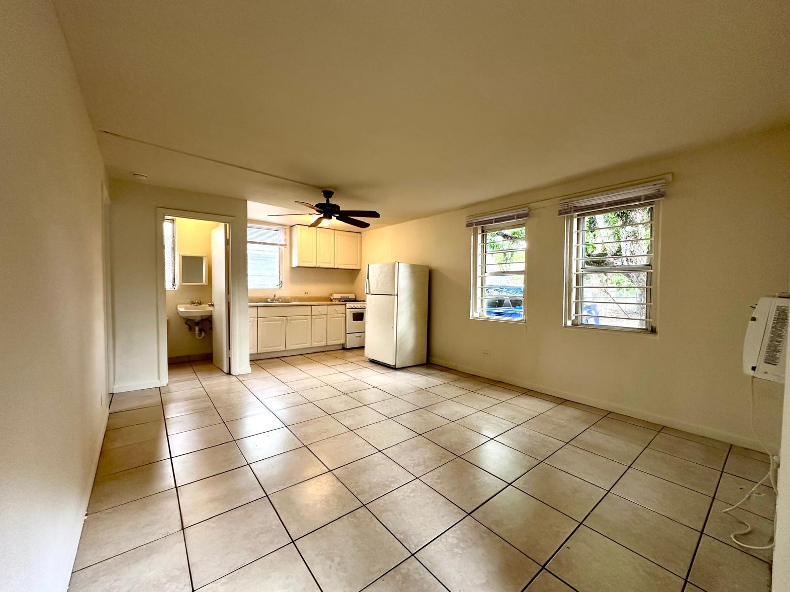 An open-concept kitchen and living area with tile floors, white cabinets, and two windows — 610 33rd Street, West Palm Beach FL 33407, WEST PALM BEACH, FL