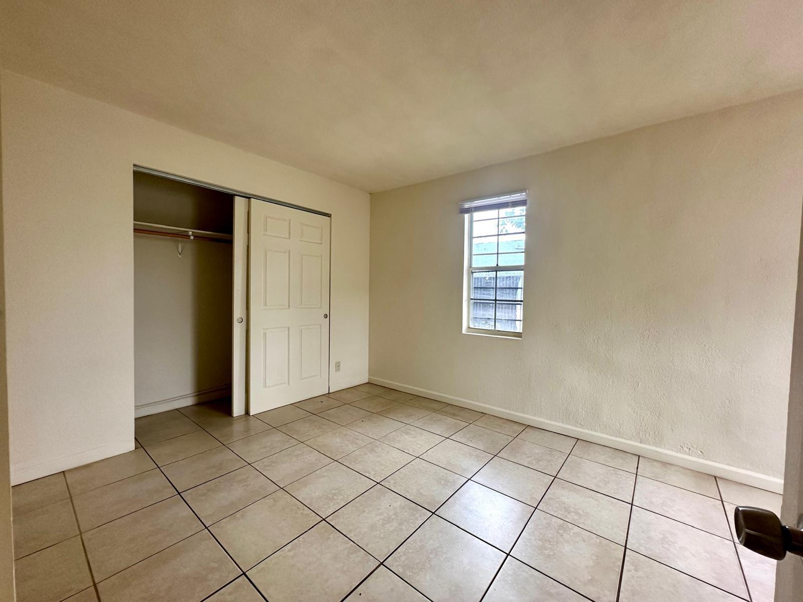 An empty bedroom features beige tile flooring, white walls, a closet, and a window — 610 33rd Street, West Palm Beach FL 33407, WEST PALM BEACH, FL