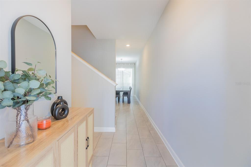 A hallway with light tile flooring leads past a staircase toward a dining area — 4806 LULLABY LANE, KISSIMMEE, FL