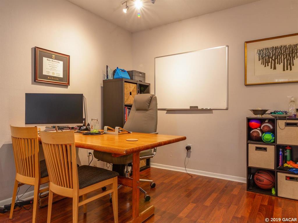 A home office features a wooden desk, two chairs, a whiteboard, and storage shelving — 1700 SW 16TH COURT UNIT D-27, GAINESVILLE, FL