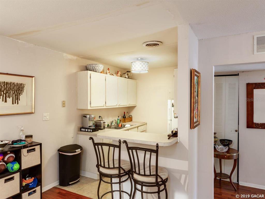 A kitchen features white cabinets, a breakfast bar with two stools, and a trash can — 1700 SW 16TH COURT UNIT D-27, GAINESVILLE, FL