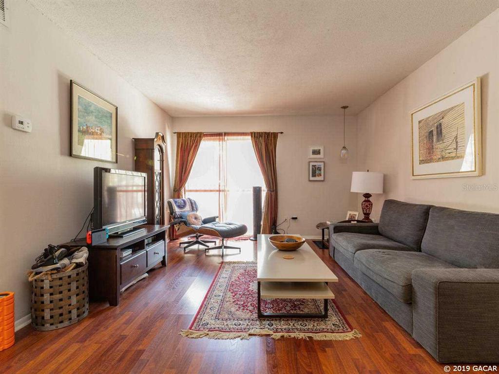A living room features wood flooring, a gray sofa, a coffee table, and a television — 1700 SW 16TH COURT UNIT D-27, GAINESVILLE, FL