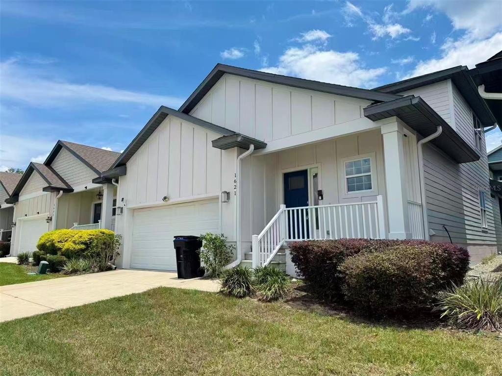 A white house with vertical siding, a garage, and a front porch under a blue sky — 1621 NW 121ST WAY, GAINESVILLE, FL