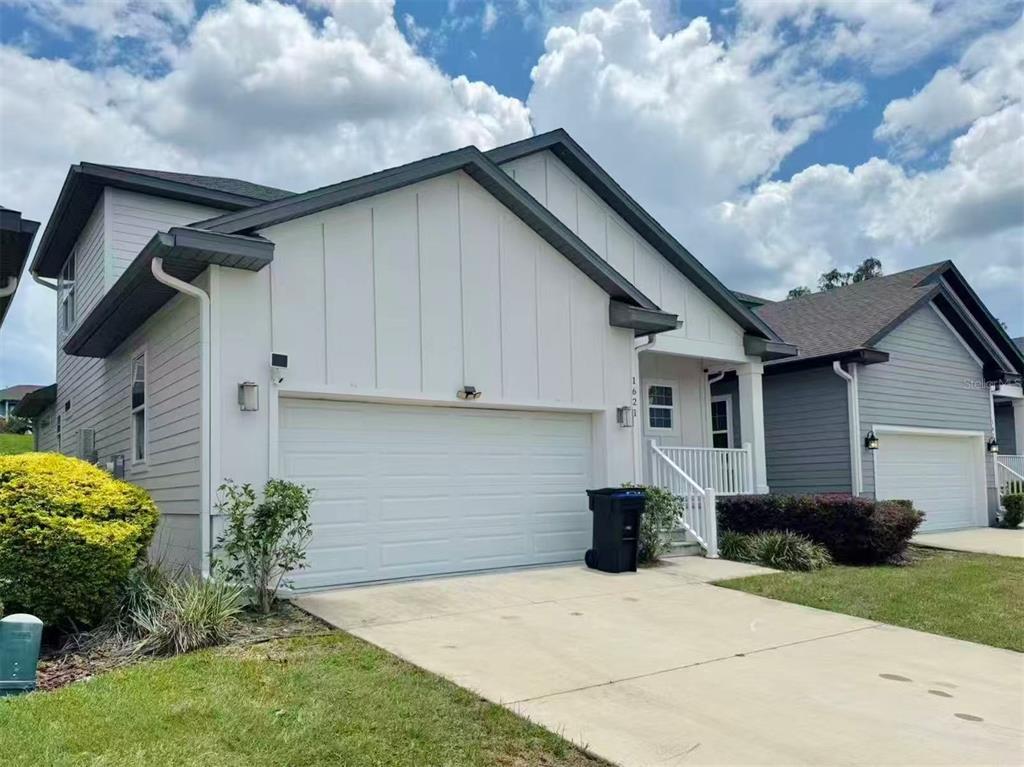 A white house with a two-car garage and a small front porch under a cloudy sky — 1621 NW 121ST WAY, GAINESVILLE, FL
