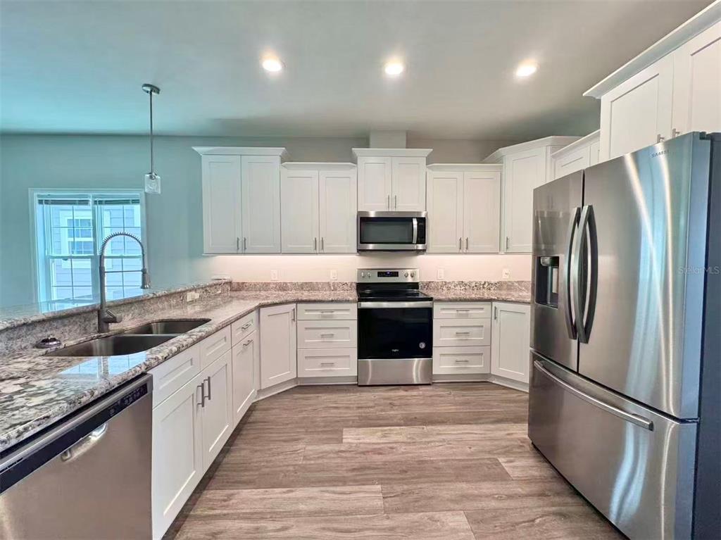 A kitchen with white cabinets, stainless steel appliances, granite countertops, and wood-look flooring — 1621 NW 121ST WAY, GAINESVILLE, FL