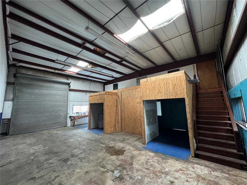 An industrial warehouse space features a concrete floor, a roll-up door, and wooden loft structures — 702 W PARK AVENUE UNIT A1, EDGEWATER, FL