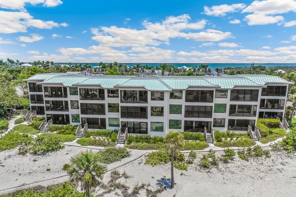 An aerial view shows a three-story beachfront apartment building with a metal roof and balconies — 5000 GASPARILLA ROAD UNIT BC202, BOCA GRANDE, FL