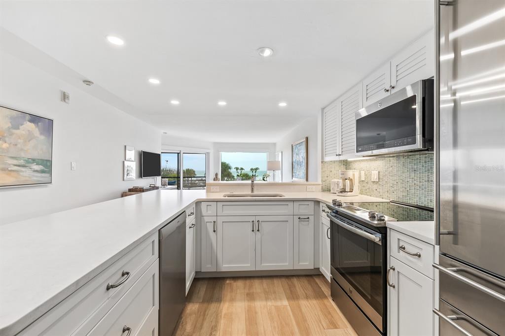 A modern kitchen features white cabinetry, stainless steel appliances, and a view of the ocean — 5000 GASPARILLA ROAD UNIT BC202, BOCA GRANDE, FL