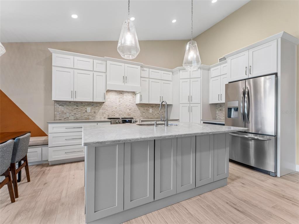 A kitchen features white upper cabinets, a gray island with a stone countertop, and stainless appliances — 3350 DUNEMOOR CT, PALM HARBOR, FL