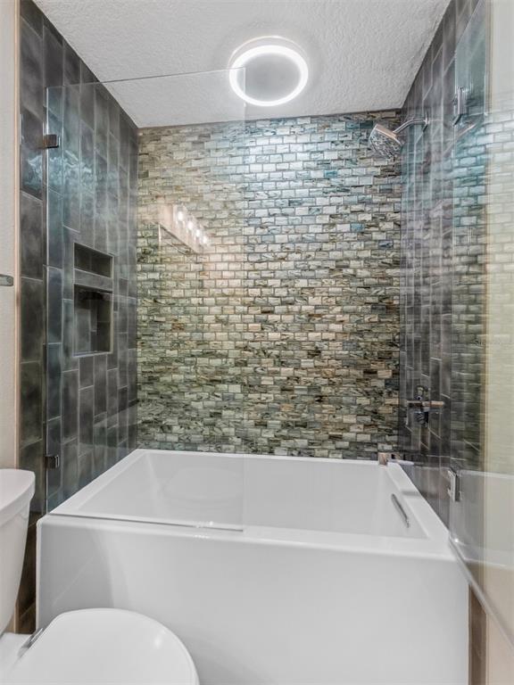 A bathroom features a white bathtub with a glass partition and decorative mosaic tile walls — 3350 DUNEMOOR CT, PALM HARBOR, FL