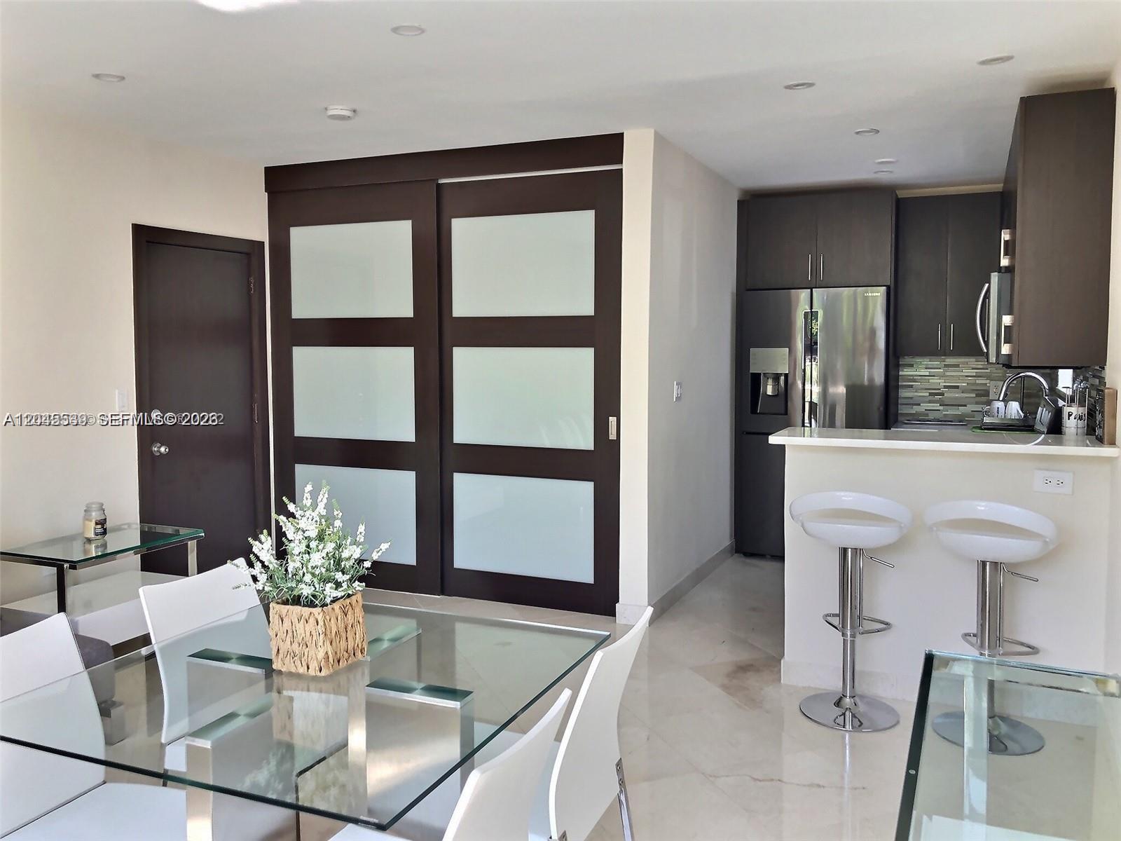 A dining area with a glass table and a kitchen with dark cabinets and bar stools — 900 Jefferson Ave # 9, Miami Beach FL 33139, MIAMI BEACH, FL