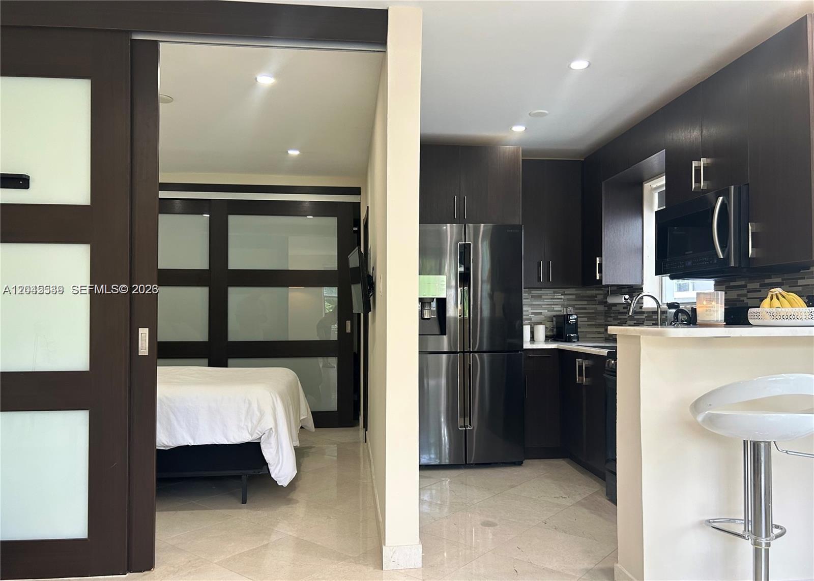 A view shows a bedroom with sliding glass doors adjacent to a modern dark-cabinet kitchen — 900 Jefferson Ave # 9, Miami Beach FL 33139, MIAMI BEACH, FL