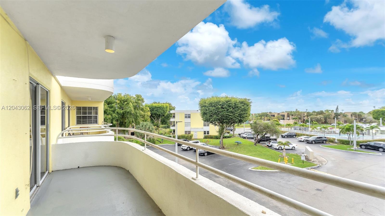 A curved balcony overlooks a parking lot, green space, and surrounding apartment buildings — 10755 SW 108th Ave # 304, Miami FL 33176, MIAMI, FL