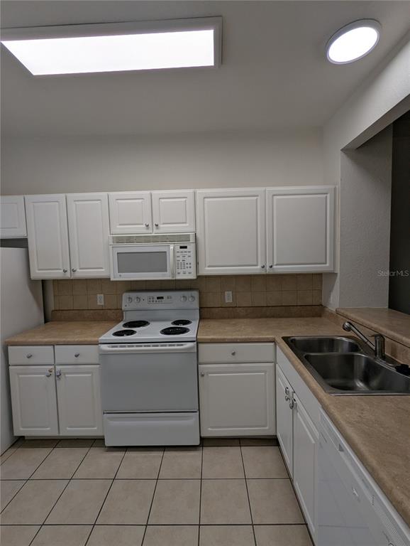 A kitchen features white cabinets, tan countertops, a white stove, and a stainless steel sink — 4833 NW 46TH PLACE UNIT 106, GAINESVILLE, FL