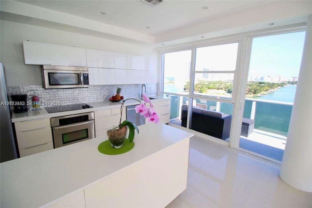 A modern kitchen features white cabinetry, stainless steel appliances, and a balcony overlooking the water — 900 Bay Dr # 1027, Miami Beach FL 33141, MIAMI BEACH, FL