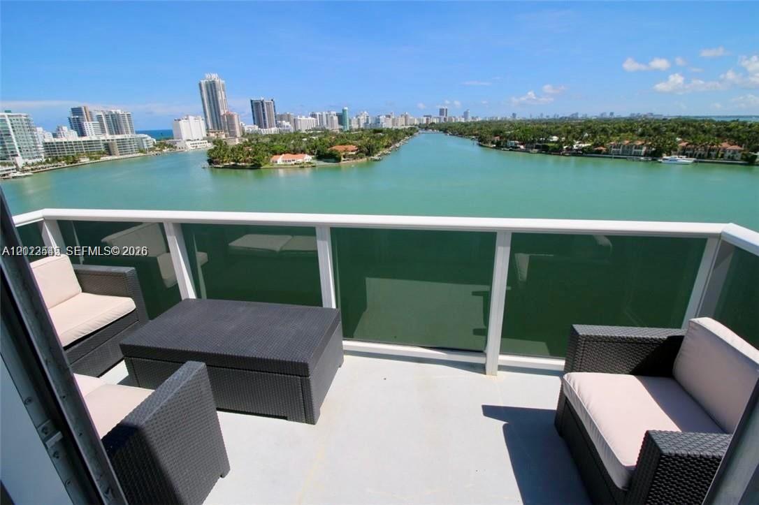 A balcony with wicker patio furniture overlooks a bay and a city skyline — 900 Bay Dr # 1027, Miami Beach FL 33141, MIAMI BEACH, FL