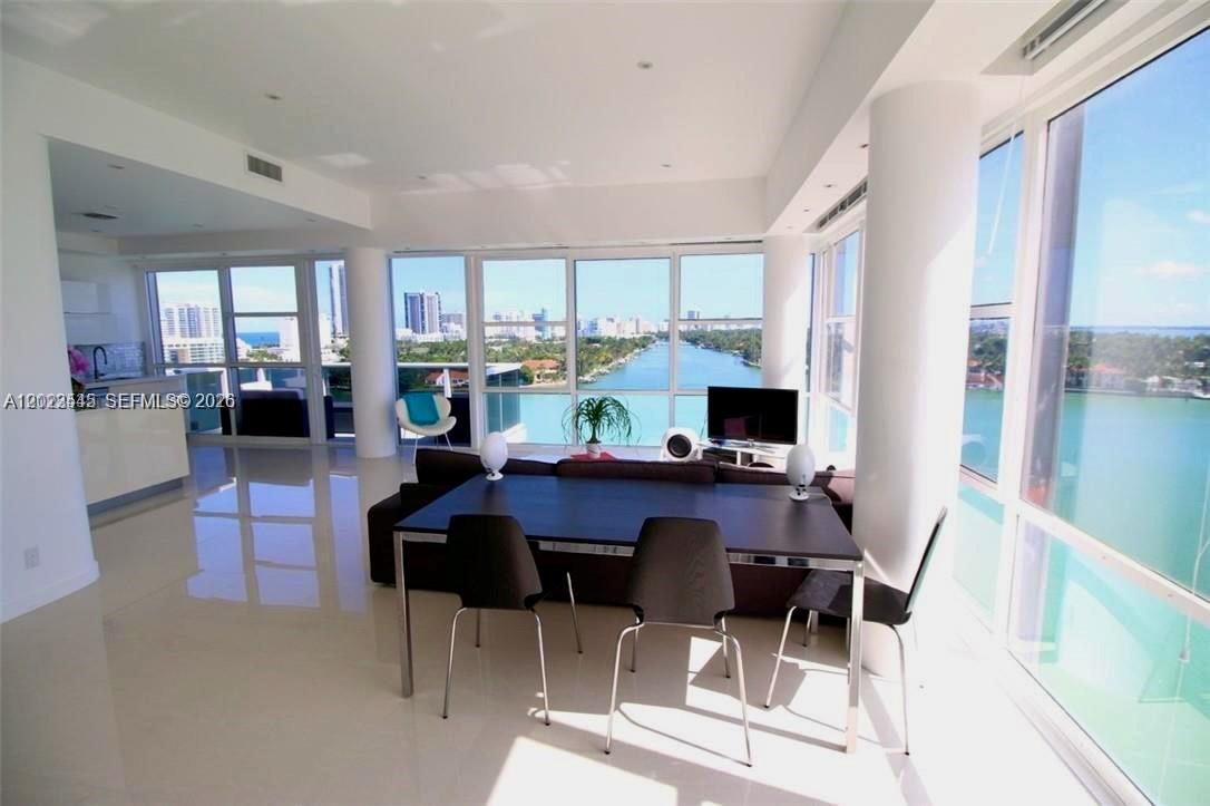 A modern living and dining area features floor-to-ceiling windows overlooking a canal and city — 900 Bay Dr # 1027, Miami Beach FL 33141, MIAMI BEACH, FL