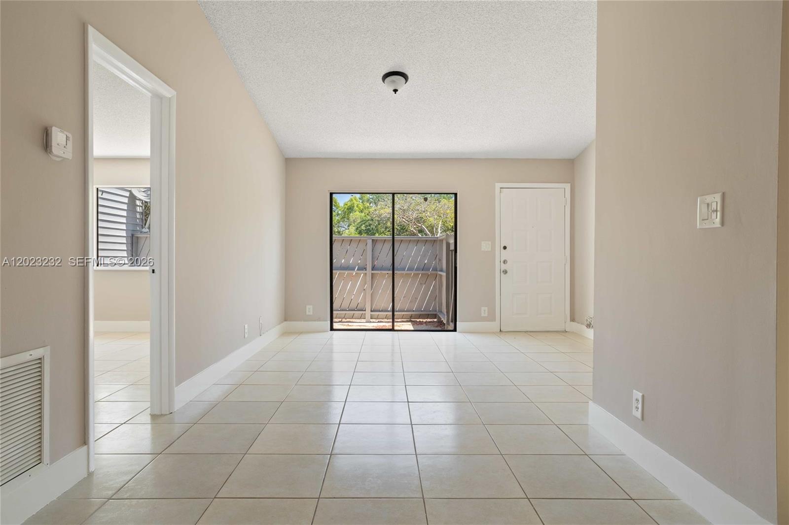 An empty room with beige tile flooring, a sliding glass door, and a white door — 3633 NW 99th Ter # 7B, Sunrise FL 33351, SUNRISE, FL