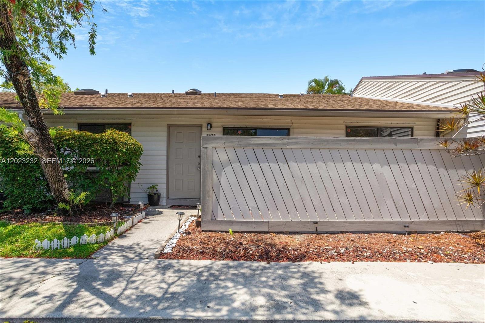 A single-story house exterior features a light-colored door, a diagonal wood fence, and landscaping — 3633 NW 99th Ter # 7B, Sunrise FL 33351, SUNRISE, FL