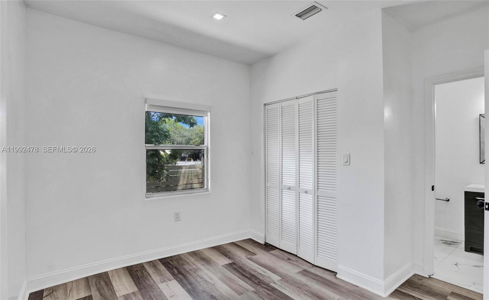 A bedroom with white walls, wood-look flooring, a window, a closet, and an attached bathroom — 2135 SW 4th St, Miami FL 33135, MIAMI, FL
