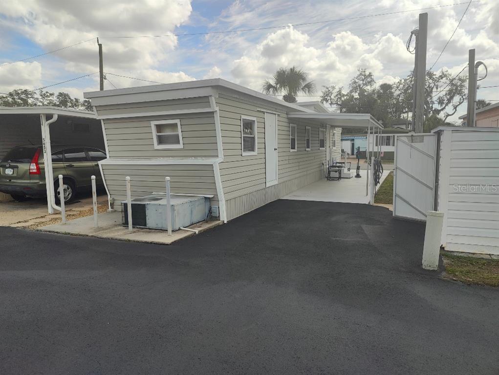 A light-colored mobile home features a carport, an adjacent driveway, and an exterior air conditioning unit — 5649 OAK RIDGE AVENUE, NEW PORT RICHEY, FL