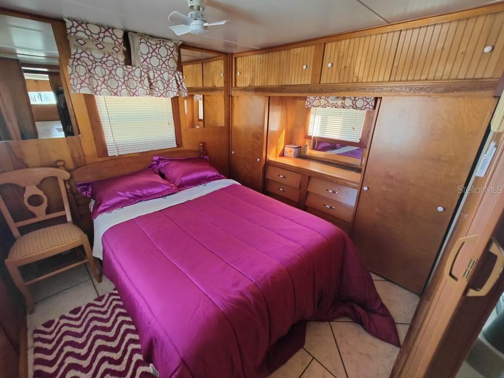 A bedroom features wood-paneled walls, a magenta bedspread, a matching rug, and built-in storage cabinets — 5649 OAK RIDGE AVENUE, NEW PORT RICHEY, FL