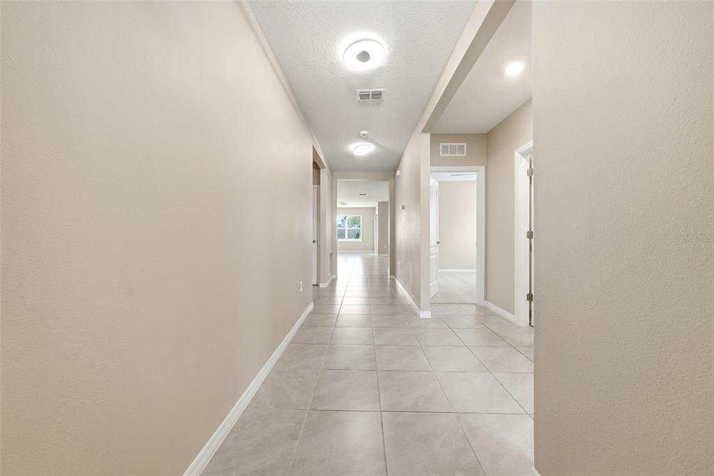 A long hallway with light-colored tile flooring and beige walls leads to an open room — 600 TALISI LOOP, ST CLOUD, FL