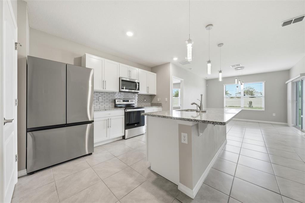 A modern kitchen features white cabinets, stainless steel appliances, granite countertops, and a center island — 600 TALISI LOOP, ST CLOUD, FL