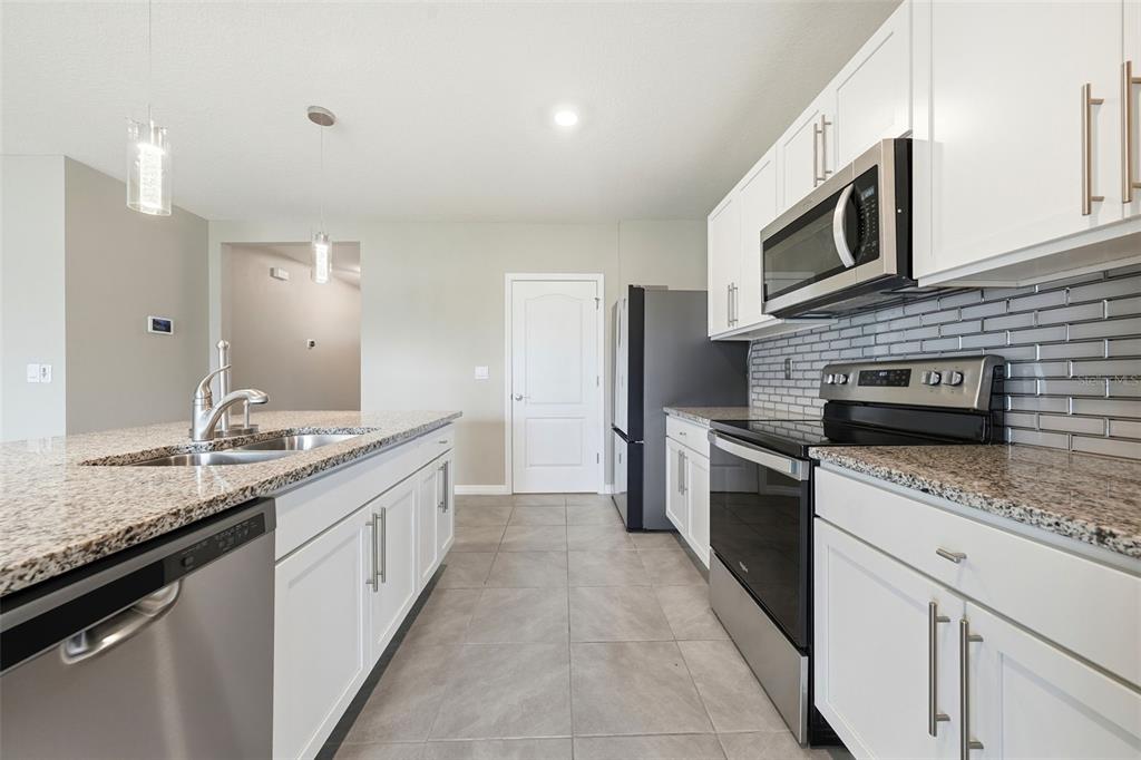 A kitchen with white cabinets, granite countertops, stainless steel appliances, and gray tile flooring — 600 TALISI LOOP, ST CLOUD, FL
