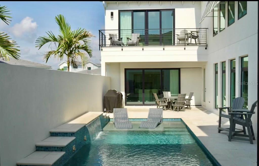 A modern home exterior features a swimming pool with a waterfall and a second-story balcony — 6003 CAT CLAW LANE, BRADENTON, FL