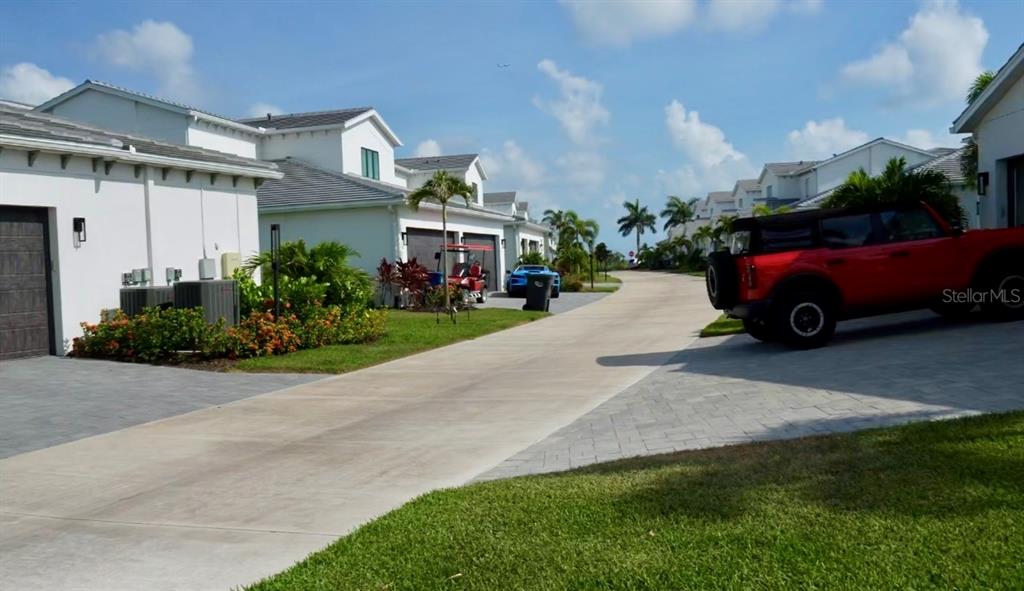 A red SUV is parked on a concrete driveway between white residential buildings — 6003 CAT CLAW LANE, BRADENTON, FL