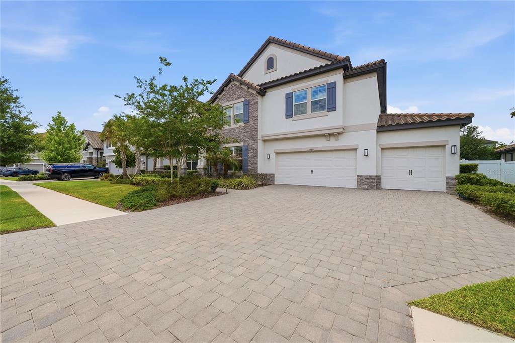 A two-story house with a stone facade, white stucco walls, and a paved driveway — 33260 KATELAND DRIVE, WESLEY CHAPEL, FL