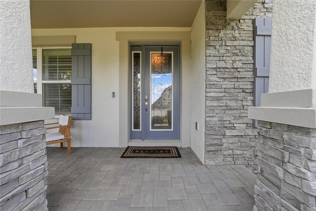 A covered front porch features a blue door with glass inserts and stone veneer accents — 33260 KATELAND DRIVE, WESLEY CHAPEL, FL