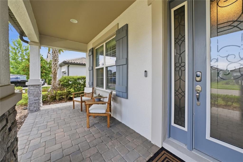 A covered front porch features paver flooring, two wooden chairs, and a blue front door — 33260 KATELAND DRIVE, WESLEY CHAPEL, FL