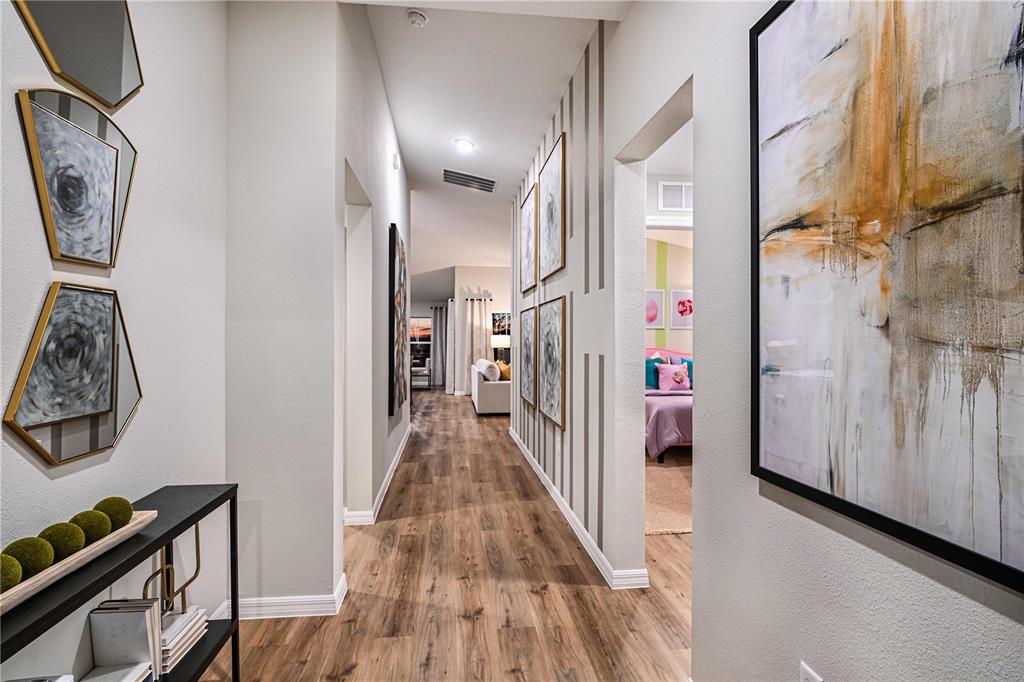 A hallway with wood-look flooring leads to a living area, featuring wall art and decor — 5832 HEAVEN ROAD, HAINES CITY, FL