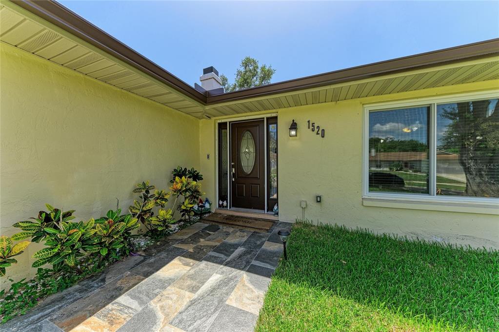 A yellow house exterior features a dark brown front door and a stone walkway — 1520 SUNNYHILLS DRIVE, BRANDON, FL