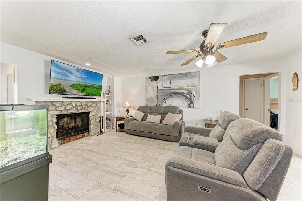 A living room features a stone fireplace, gray reclining furniture, and light-colored tile flooring — 1520 SUNNYHILLS DRIVE, BRANDON, FL