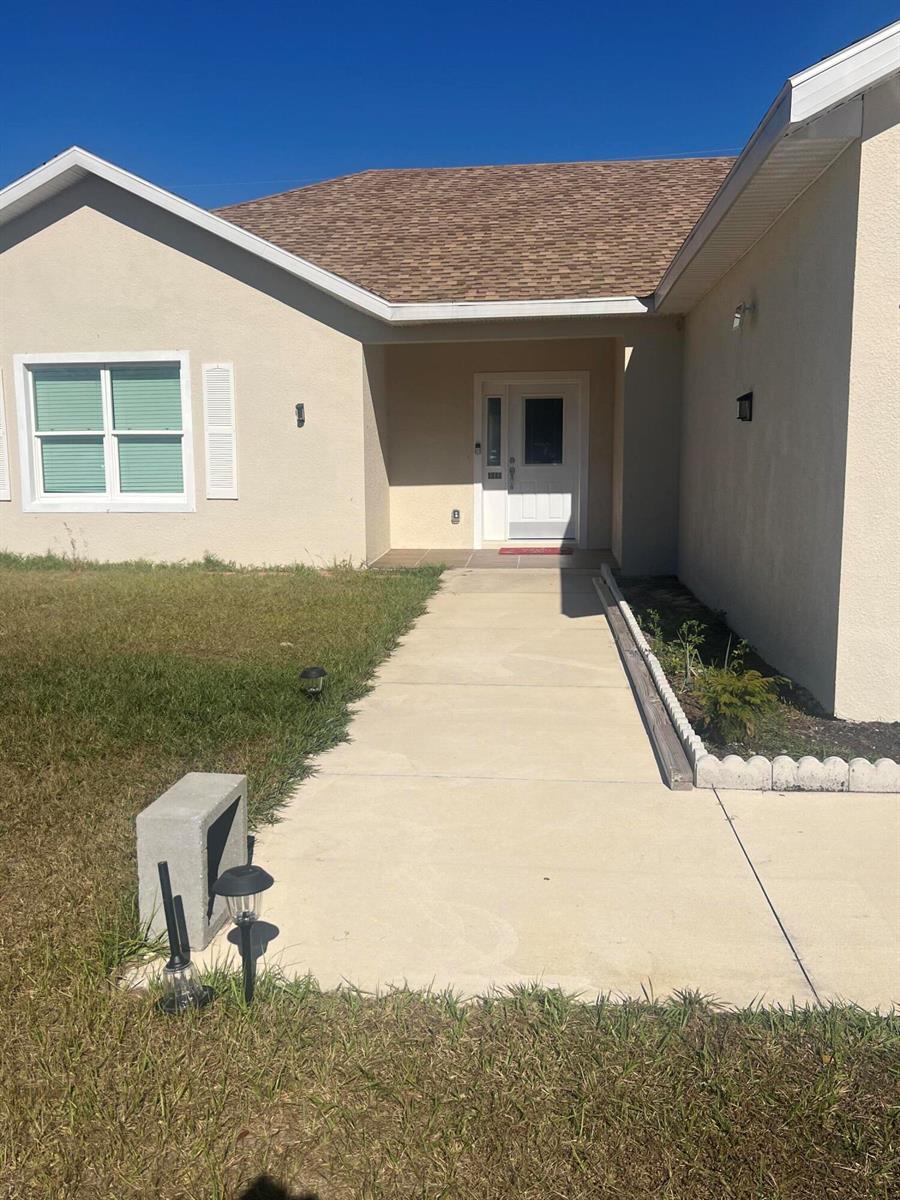 A beige house exterior features a concrete walkway leading to a white front door — 4009 SW 133rd Loop, Ocala FL 34473, OCALA, FL
