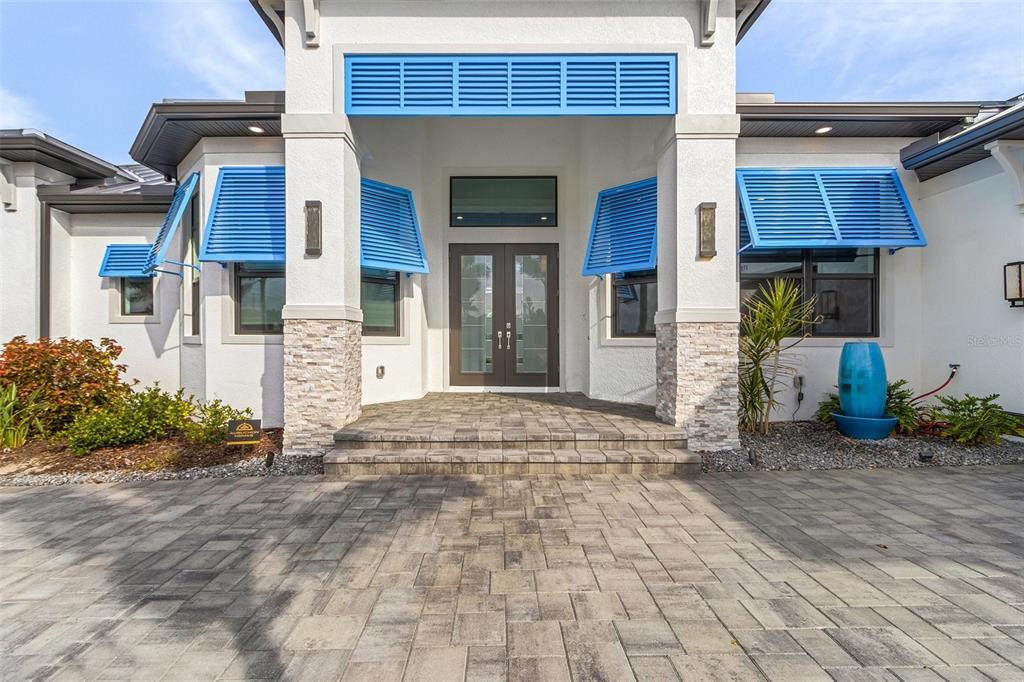 A modern home entrance features a stone-accented porch, double doors, and bright blue louvered shutters — 1729 NW 41ST AVENUE, CAPE CORAL, FL