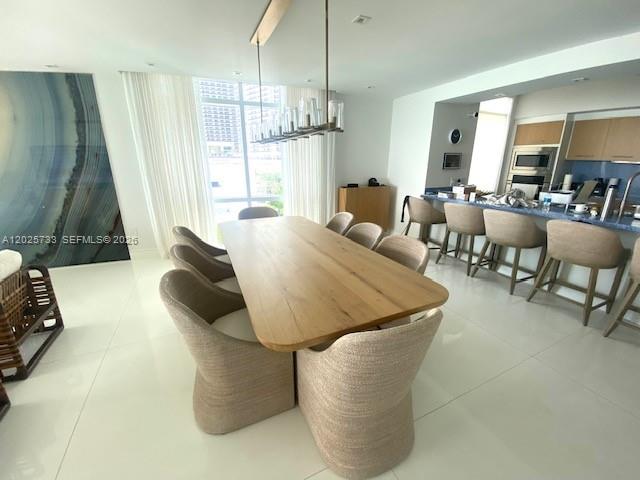 A modern dining area features a long wooden table, upholstered chairs, and a kitchen island — 3951 S Ocean Dr # 501, Hollywood FL 33019, HOLLYWOOD, FL